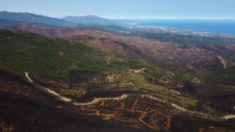 A-drone-pulls-back-over-a-burnt-mountainside-and-road-near-Estepona,-Spain