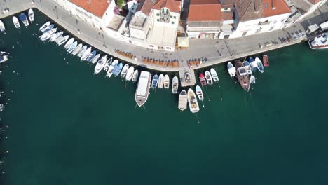 Aligned-fishing-boats-moored-to-the-quays-of-Milna-Town-harbor-against-white-limestone-houses,-Brac-Island