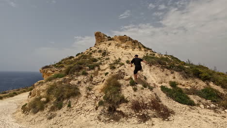 Slow-motion---Caucasian-man-runs-up-sandy-mound-on-cloudy-day-by-sea