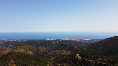 A-drone-pulls-back-revealing-a-mountain-road-leading-to-the-shoreline-of-Estepona,-Spain