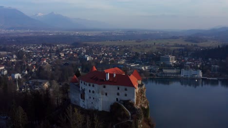 Aerial-Flying-Towards-Lake-Bled-Castle-With-Snow-Capped-Karawanks-In-Background