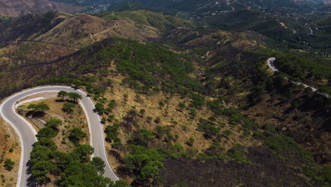 A-drone-tilts-up-revealing-an-aerial-of-a-winding-road-leading-to-the-coast-of-Estepona,-Spain