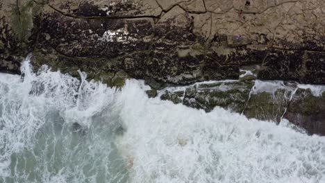 Aerial-drone-birds-eye-top-view-medium-shot-of-small-waves-crashing-into-algae-covered-rocks-on-the-tropical-Tibau-do-Sul-beach-during-high-tide-in-Rio-Grande-do-Norte,-Brazil-on-a-warm-summer-day