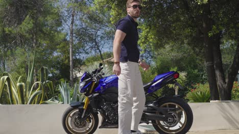 Slow-motion-shot-of-a-motorbike-rider-wearing-glasses-dismounting-his-bike-on-the-drive