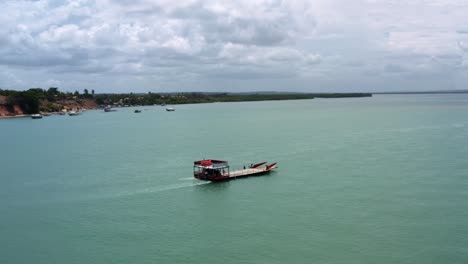 Aerial-drone-shot-rotating-around-a-large-red-ferry-transport-boat-carrying-a-car-across-the-Malembá-crossing-of-the-Guaraíras-Lagoon-in-Tibau-do-Sul-near-Pipa,-Brazil-in-Rio-Grande-do-Norte
