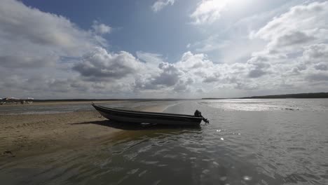 A-small-lone-motorboat-docked-on-the-large-sand-bar-during-low-tide-in-the-Guaraíras-Lagoon-of-Tibau-do-Sul,-Brazil-in-Rio-Grande-do-Norte-near-Pipa-on-a-warm-sunny-cloudy-summer-day