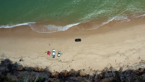 Aerial-drone-birds-eye-top-view-shot-following-a-car-drying-down-the-tropical-Malembá-beach-with-golden-sand-and-calm-crystal-clear-turquoise-water-near-Tibau-do-Sul-in-Rio-Grande-do-Norte,-Brazil