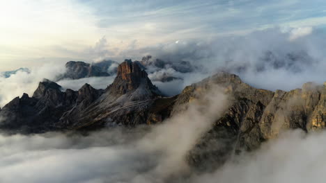 Panoramic-drone-shot-of-low-hanging-clouds-surrounding-rocky-peaks-of-Dolomites,-Italy