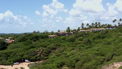 Dolly-out-aerial-drone-shot-of-a-beautiful-luxurious-hotel-surrounded-by-exotic-foliage-on-the-large-hill-of-the-famous-tourist-beach-town-of-Pipa,-Brazil-in-Rio-Grande-do-Norte-on-a-sunny-summer-day