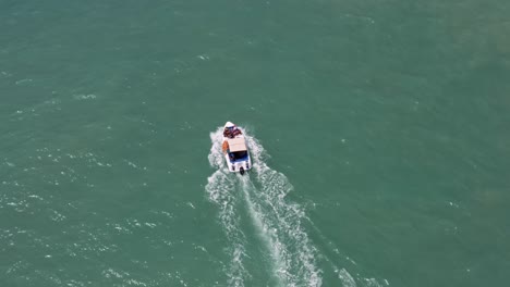 Aerial-drone-birds-eye-top-view-following-a-small-dolphin-tour-boat-sailing-in-tropical-turquoise-ocean-water-with-tourists-near-Madeiro-beach-in-Pipa,-Brazil-Rio-Grande-do-Norte-on-a-warm-summer-day
