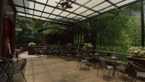 Hermosa-Terraza-De-Madera-De-Una-Cafetería-Con-Vistas-Al-Exuberante-Parque-Boscoso-Con-Un-Lago-En-Un-Día-Soleado