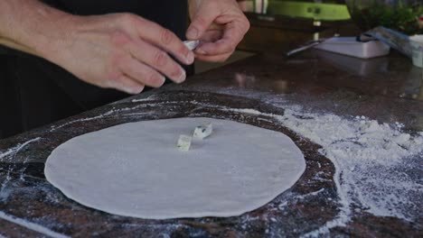 Chef-Agregando-Coberturas-De-Queso-A-La-Pizza-En-Una-Cocina-Rústica-Al-Aire-Libre