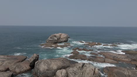 Calm-ocean-water-at-coastal-rocks,-aerial-with-horizon-over-water
