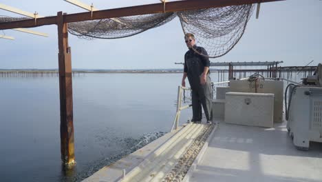 Conchyliculteur-En-Su-Barco,-Desplegando-Una-Red-Llena-De-Ostras-En-El-Mar,-Mostrando-Mesas-De-Metal-Que-Sostienen-Los-Mariscos