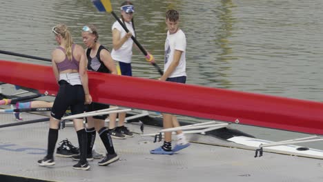 A-group-of-female-competitors-and-their-coach-bring-a-quadruple-scull-to-the-pier-and-carefully-place-it-on-the-water
