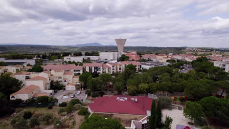 Aerial-View-of-the-Massane-Heights-of-Montpellier,-featuring-a-Water-Tower-and-the-Pic-St-Loup-Mountain-in-the-Background,-with-Overcast-Gray-Clouds-Filling-the-Sky