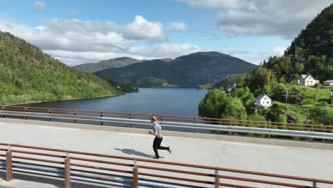 Man-running-across-bridge-over-scenic-fjord,-Norway