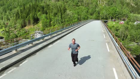 Aerial-reverse-dolly-of-man-jogging-over-bridge-in-Norway