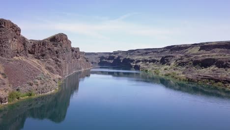 Low-flight-over-Deep-blue-lake-with-vertical-cliffs-in-arid-landscape