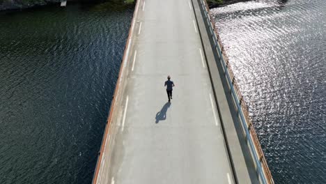 Die-Sonne-Glitzert-Auf-Dem-Wasser,-Während-Ein-Mann-Auf-Einer-Brücke-über-Den-Norwegischen-Fjord-Joggt