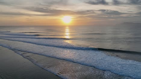 Panning-drone-clip-of-yellow-gold-sunset-over-calm-ocean-waters,-moving-to-show-tip-of-island-of-Java,-Indonesia-and-dense-rainforest