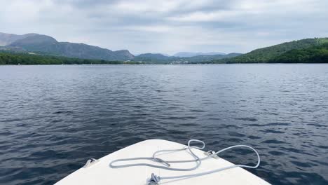 A-forward-facing-POV-view-of-the-bow-of-a-small-white-motor-boat-driving-along-Coniston-Water-in-the-Lake-District,-UK