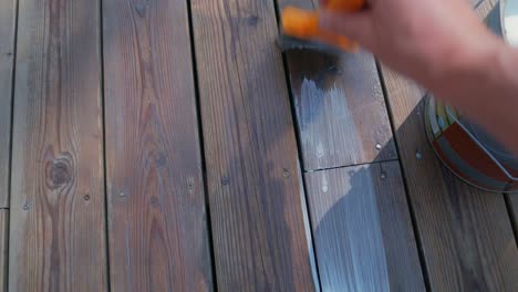 Male-hand-use-paint-brush-to-apply-wooden-oil-to-the-decking