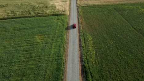 Revealing-drone-shot-of-a-lone-red-car-driving-on-a-narrow-road-through-agricultural-land,-Poland