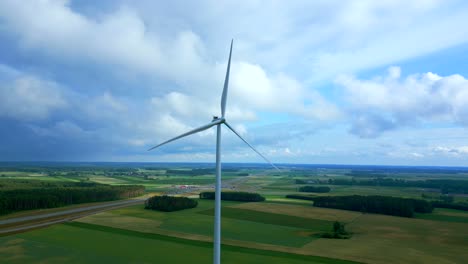 Luftaufnahme-Einer-Windkraftanlage,-Die-Sich-Langsam-Auf-Einem-Windmühlen-Energiepark-Auf-Landwirtschaftlichen-Feldern-Mit-Geschwollenen-Wolken-Dreht,-Polen