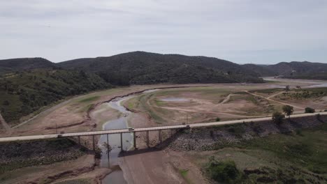 Bridge-over-dry-Arade-River-and-green-hills-in-Portugal,-aerial-pan