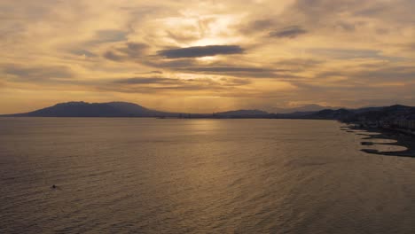 Drohnenclip-Eines-Ruhigen-Bootshafens-Und-Der-Küste-Mit-Bergen-Im-Hintergrund,-Bei-Sonnenuntergang-Zur-Goldenen-Stunde