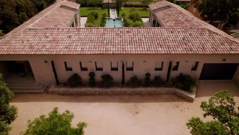 Aerial-View-of-a-Provençal-Roman-Style-Villa-with-a-Courtyard,-Pool,-and-Garden,-Revealing-an-Olive-Grove-through-a-Tilted-Drone-Shot