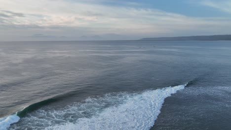 Panning-drone-clip-from-golden-sunset-moving-left-to-right-over-perfect-surf-waves-towards-dense-jungle-and-shoreline-of-Grajagan-bay,-Java,-Indonesia