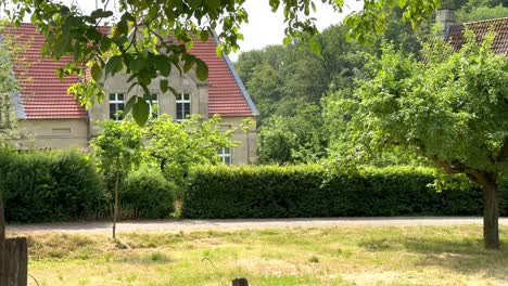 Schwenkaufnahme-Eines-Wunderschönen-Gartens-Und-Eines-Alten-Westfälischen-Bauernhauses-Mit-Luxuriöser-Sandsteinfassade-An-Einem-Sonnigen-Tag-In-Deutschland