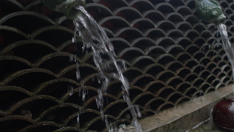 Stylized-fountain-in-form-of-a-fish-mounted-into-wall-pouring-water-into-the-jug-below