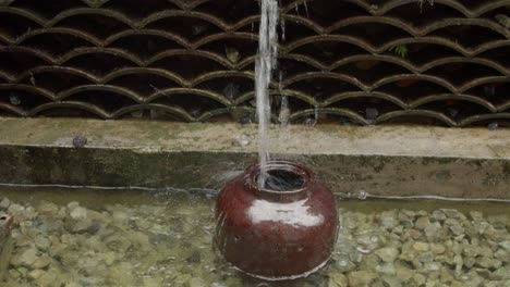 Stylized-fountain-in-form-of-a-fish-mounted-into-wall-pouring-water-into-the-jug-below