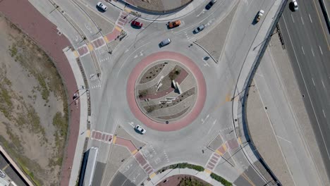 Top-down-drone-rotation-over-a-busy-roundabout-with-diverse-vehicles-in-early-afternoon,-slowly-rotating-anti-clockwise