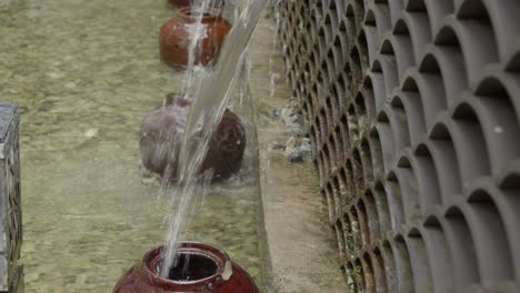 Stilisierter-Brunnen-In-Form-Eines-In-Die-Wand-Montierten-Fisches,-Der-Wasser-In-Den-Darunter-Liegenden-Krug-Gießt