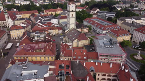 Drone-tilt-up-reveal-past-iconic-clock-tower-in-Klagenfurt,-Carinthia,-Austria