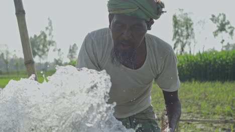 Unbekannter-Bauer-Spritzt-Ihm-Wasser-Ins-Gesicht,-Um-Ihn-Sauber-Zu-Waschen,-Während-Die-Wasserpumpe-Auf-Hochtouren-Läuft