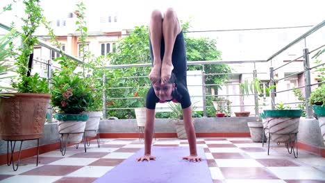A-front-view-of-a-very-young-girls-doing-handstand-poses-with-both-hands-on-her-back-in-her-terrace-garden