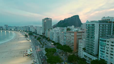 Aerial-view-establishing-the-traffic-on-the-Copacabana-waterfront-with-the-sunset-in-the-background-in-Rio-de-Janeiro-Brazil,-buildings-in-front-of-the-beach