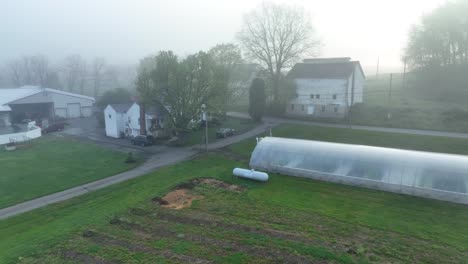 Aerial-view-of-foggy-allotment-with-plastic-greenhouse-and-white-houses
