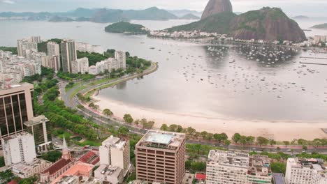 Aerial-orbit-of-Botafogo-beach-in-Rio-de-Janeiro-Brazil-with-the-sugarloaf-and-many-parked-yachts,-curve-along-the-beach