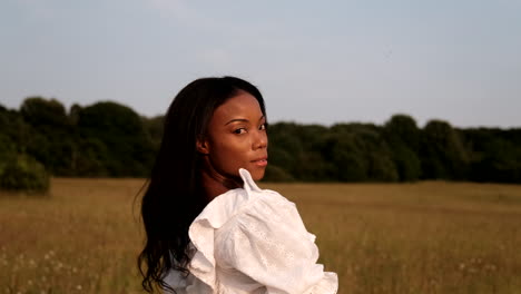 Black-woman-flicks-hair-back-looking-straight-into-camera-as-sun-hits-her-face-while-standing-on-a-field-during-a-warm-sunny-day