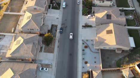 A-serene-drone-shot-traces-a-car-navigating-through-a-quiet-suburban-neighborhood,-concluding-as-it-ventures-into-the-glorious-golden-hour-sunset