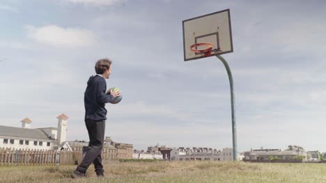 Adult-male-playing-basketball-by-himself-at-outdoor-court-during-daytime