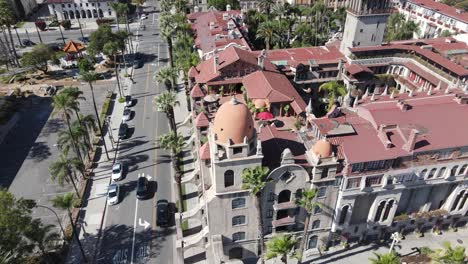 A-sweeping-drone-shot-orbits-the-historic-Mission-Inn-Hotel-and-Spa-in-Riverside,-CA,-with-the-busy-downtown-and-the-91-highway-serving-as-the-backdrop