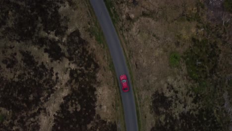 Top-down-view-of-red-car-being-driven-round-a-bend-of-single-track-road