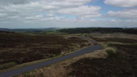 Red-car-tracked-by-drone-along-a-single-track-road-in-the-countryside